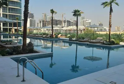 a large swimming pool with palm trees and buildings at Modern 1BR Hideaway In Binghatti Phoenix-JVC in Dubai