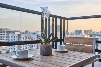 a wooden table with two cups and a flower on a balcony at Joya Blanca Residence - Bright 1BR Apartment in Arjan in Dubai