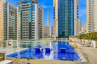 a large swimming pool with chairs and tall buildings at Bayz by Denube in Dubai