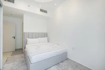 a bed in a room with a white wall at Luxury 1BR Apartment in Binghatti Mirage JVC Dubai in Dubai