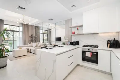 a kitchen with white cabinets and a living room at Luxury 1BR Apartment in Binghatti Mirage JVC Dubai in Dubai
