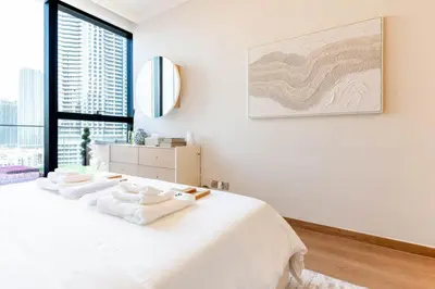 a white bedroom with a large bed and a large window at 1BR Plus Studio Apartment With Burj View In Downtown Dubai in Dubai