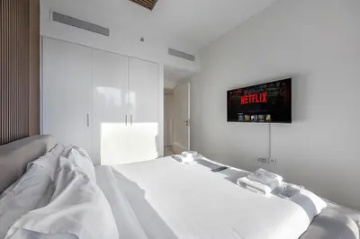 a white bedroom with a bed and a tv on the wall at Burj Khalifa Views Pool, Gym & Downtown Ease in Dubai