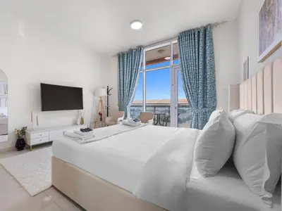 a white bedroom with a large bed and a large window at Modern Comfort City Studio In Al Manara 04 in Dubai