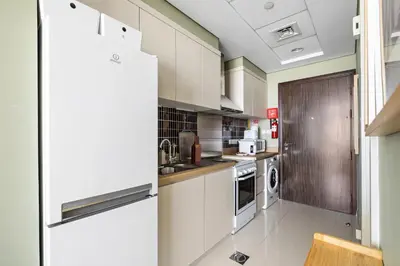 a kitchen with white cabinets and a refrigerator at Stylish Studio with Balcony in Carson Tower, DAMAC Hills in Dubai