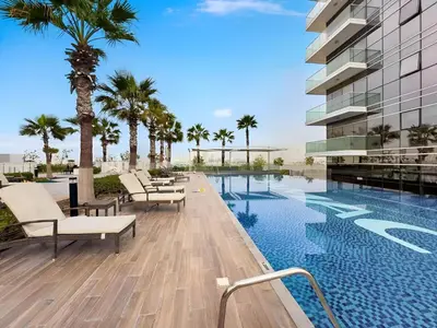 a pool with chairs and palm trees next to a building at Stylish Studio with Balcony in Carson Tower, DAMAC Hills in Dubai