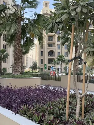 a garden with palm trees and purple flowers in front of a building at Luxury 1BR Retreat with Dubai Marina views by Crescent Key in Dubai