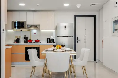 a kitchen with a table with white chairs and a kitchen at FIRST CLASS 1BR Miracle Garden View Skyz Arjan in Dubai
