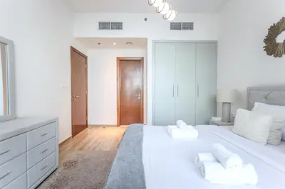 a white bedroom with a large white bed with white pillows at Elite LUX Holiday Homes - Stylish 1BR Living in Amna Tower, Al Habtoor City in Dubai
