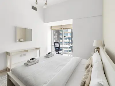 a white bedroom with a bed with a desk and a chair at Skyline Marina - Modern 2BR Retreat In Cayan-33 in Dubai