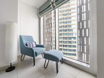 a chair and stool in a room with a large window at Skyline Marina - Modern 2BR Retreat In Cayan-33 in Dubai