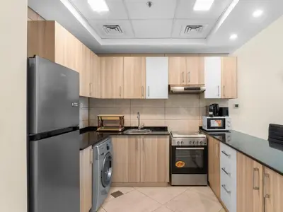 a kitchen with wooden cabinets and a stainless steel refrigerator at The Cozy Corner Studio In Chaimaa in Dubai