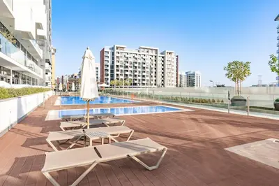 a patio with chairs and an umbrella and a pool at Elegant 1BR Near Downtown Azizi Riviera 3 in Dubai