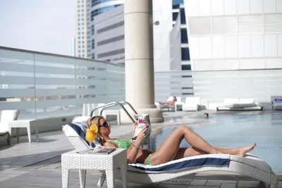 a woman laying in a chair reading a book next to a pool at Social Hotel in Dubai