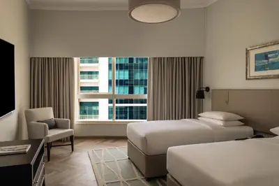 a hotel room with two beds and a chair and a window at Dubai Marriott Harbour Hotel And Suites in Dubai