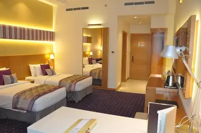 a hotel room with two beds and a desk at Fortune Park Hotel in Dubai