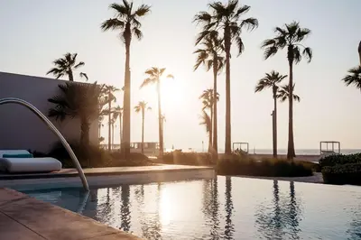 a swimming pool with palm trees and the ocean at Nikki Beach Resort & Spa Dubai in Dubai