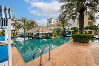 a swimming pool with palm trees and a building at Al Habtoor Polo Resort in Dubai