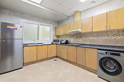 a kitchen with wooden cabinets and a washer and dryer at Al Khoory Hotel Apartments Al Barsha in Dubai