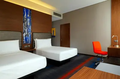 a hotel room with two beds and a red chair at Aloft Me'aisam, Dubai in Dubai