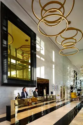 a lobby with a large chandelier and two people at Millennium Atria Business Bay in Dubai