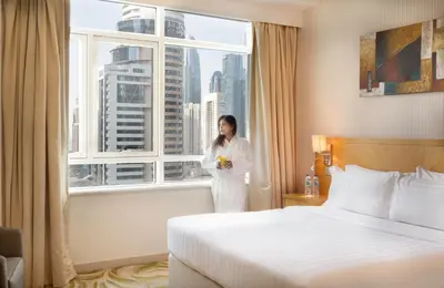 a woman standing in a hotel room with a window at Oaks Liwa Heights Hotel Suites in Dubai