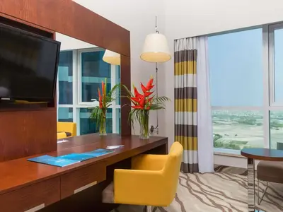 a room with a desk with a tv and a yellow chair at Novotel Dubai Al Barsha in Dubai