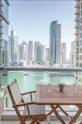 a wooden table and chair on a balcony with a view of a city at Nasma Luxury Stays - Pastel-Colored Apt With Jaw-Dropping Marina Views in Dubai