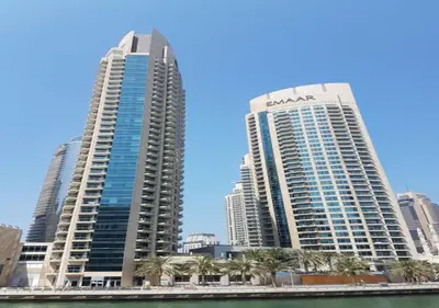 two tall buildings with palm trees in front of a city at Nasma Luxury Stays - Pastel-Colored Apt With Jaw-Dropping Marina Views in Dubai