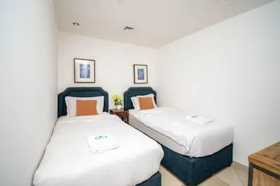 two beds in a room with white sheets and orange pillows at Stylish and Sleek 1 Bed + Study near the JBR beach in Dubai
