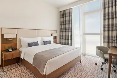 a hotel room with a large bed and a desk and a chair at Staybridge Suites Dubai Al-Maktoum Airport by IHG in Dubai