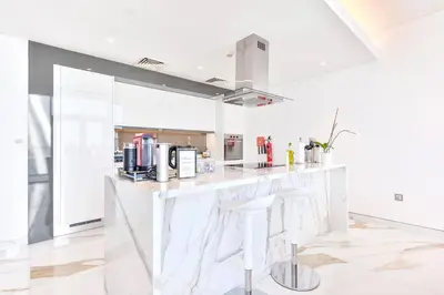 a white kitchen with white counter tops and stools at Lavish & Equipped oceanfront 2 BR facing Ain Dubai in Dubai