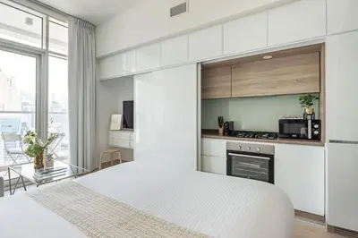 a white bedroom with a bed and a kitchen at Frank Porter - Studio One in Dubai
