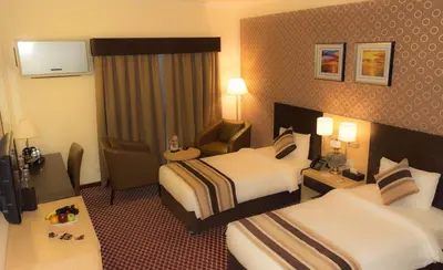 a hotel room with two beds and a chair at Fortune Karama Hotel in Dubai