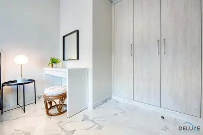 a white room with a stool and a white cabinet at Distance Away From Expo City Dubai 1BR Unit, MAG 510, Madinat Al Mataar by Deluxe Holiday Homes in Dubai
