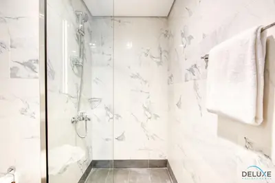 a bathroom with a shower with white marble walls at Distance Away From Expo City Dubai 1BR Unit, MAG 510, Madinat Al Mataar by Deluxe Holiday Homes in Dubai