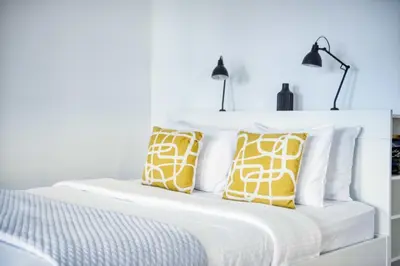 a white bed with yellow and white pillows on it at The Smart Concierge - Discovery Gardens street 4 in Dubai