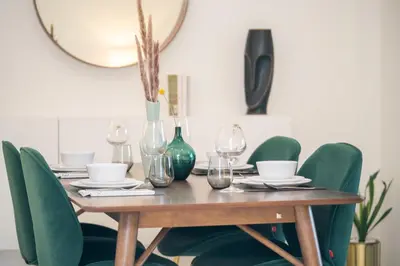 a dining room table with green chairs and a mirror at HiGuests - Chic Apt with Balcony and Pool near Burj Khalifa in Dubai