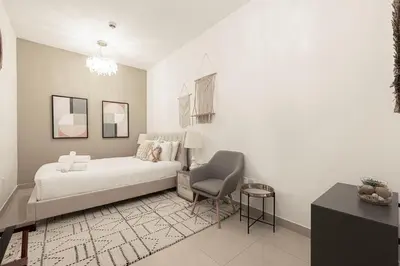 a white bedroom with a bed and a chair at FIRST CLASS 3BR Burj Khalifa & Fountain View in Dubai