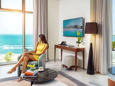 a woman sitting in a chair with a laptop in a living room at Th8 Palm Dubai Beach Resort, Vignette Collection by IHG in Dubai
