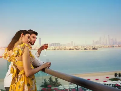 a man and a woman standing on a balcony with a drink at Th8 Palm Dubai Beach Resort, Vignette Collection by IHG in Dubai