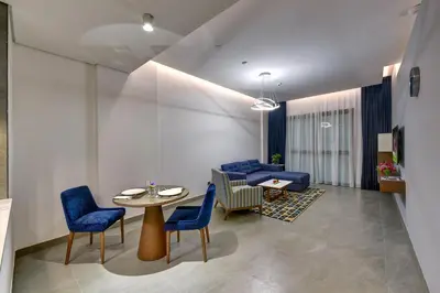 a living room with a table and blue chairs at ABAR HOTEL APARTMENTS DIP-1 in Dubai