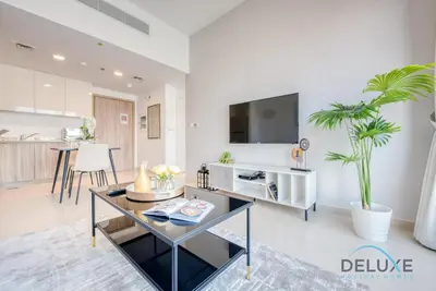 a living room with a table and a tv on a wall at Chic 1BR in Town Square UNA Dubailand by Deluxe Holiday Homes in Dubai