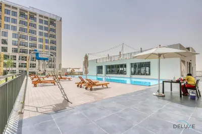 a pool with benches and an umbrella and a playground at Chic 1BR in Town Square UNA Dubailand by Deluxe Holiday Homes in Dubai