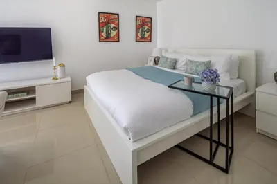 a white bedroom with a bed and a tv at Frank Porter - The Medalist in Dubai