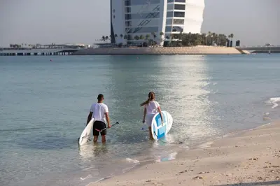 a man and a woman walking in the water with surfboards at Jumeirah Dar Al Masyaf Dubai in Dubai