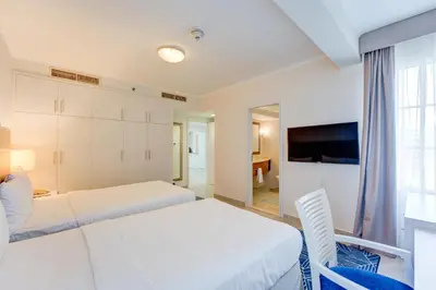 a white bedroom with two beds and a television at Millennium Lakeview Residences in Dubai