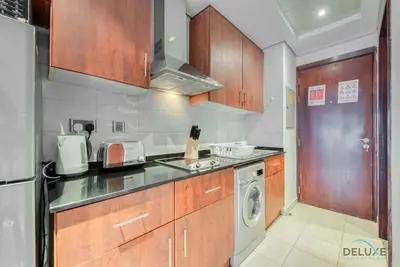 a kitchen with wooden cabinets and a washer and dryer at Calm Studio at Lake View Tower JLT by Deluxe Holiday Homes in Dubai
