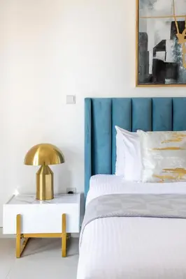a bed with a blue headboard and a gold lamp on a side table at Frank Porter - The Pulse Residences in Dubai