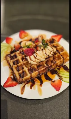 a plate of waffles and fruit on a table at SITARA HOTEL APARTMENT in Dubai